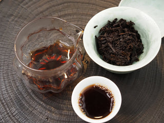 Complete Chinese Gongfu tea session setup for 2019 Dayi 7592 ripe puerh, featuring a glass pitcher, teacup, and celadon brewing bowl.