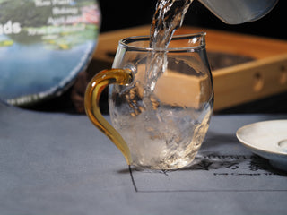 Pouring clear and lively Sheng Puerh tea liquor from a Gaiwan into a glass sharing pitcher.