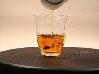 Deep amber tea liquor from 2014 aged White Peony waffle cake poured from a gaiwan into a glass fairness pitcher.