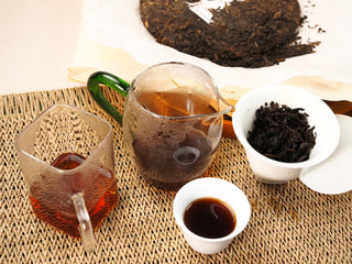 Gongfu brewing scene of 2020 Bojun Ripe Pu-erh: two pitchers, gaiwan with infused leaves, tasting cup, and the cake.
