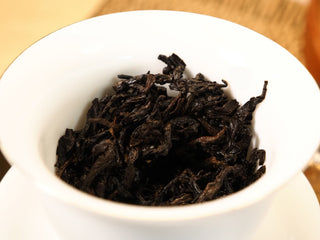 Wet leaf of Bojun Ripe Pu-erh 7.0 after multiple steepings, dark brown fermented leaves fully opened in a white porcelain gaiwan.