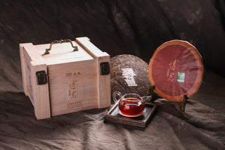 Wooden gift box with Bojun 2019 engraving beside the wrapped 2019 Bojun 500g cake, with a glass pitcher of red tea.
