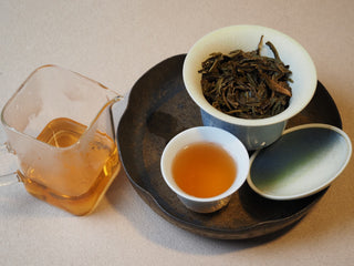 Complete tea tasting setup with gaiwan, fair cup, tasting cup, and clear golden raw puerh tea liquor.