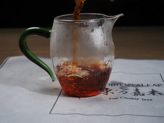 Pouring the dark reddish-brown brewed tea liquor of 2006 Dayi 7572 into glass pitcher