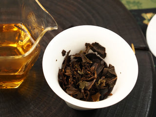 Dark wet leaves of 2014 Fuding White Peony waffle cake in a gaiwan beside a pitcher pouring amber tea liquor.