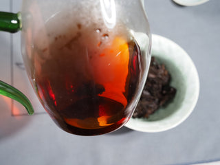 Steaming hot and clear burgundy-red ripe Puerh tea liquor being poured from glass pitcher