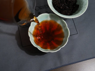 A cup of vibrant ruby-red aged 2006 Dayi 7572 ripe Puerh tea soup in a white porcelain cup