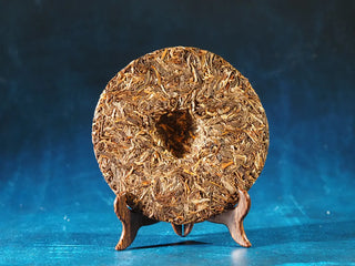 Back view of 2023 Menghai First-Flush Golden Abundance Raw Puerh Tea Cake (357g) without packaging, showing uniform compressed shape and silver-tipped leaves.