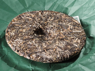 2023 Menghai First-Flush Golden Abundance Raw Puerh Tea Cake (357g) placed on packaging paper, ready to be broken apart, highlighting craftsmanship.