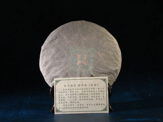 2023 Menghai First-Flush Golden Abundance Raw Puerh Tea Cake (357g) unwrapped alongside the product card, showing hand-pressed tea leaves and silver tips.