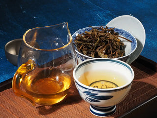 Close-up of 2023 Menghai First-Flush Golden Abundance Raw Puerh Tea (357g) with gaiwan, fair cup, and tasting cup together, showing brewed leaves and bright tea liquor.