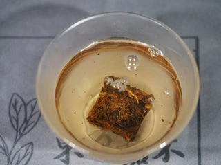 Golden Flower White Tea mini-cake "blooming" in hot water, starting the steeping process in a glass.