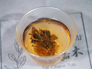 Fully bloomed loose leaf texture of the Golden Flower White Tea (mini-cake fully opened) in the glass brewing vessel.