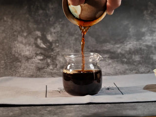 Golden Treasure Ripe Puerh Tea Cake – Menghai Origin, brewed tea being poured from the gaiwan into a glass fairness cup, showcasing deep ruby-red liquor reminiscent of red wine.