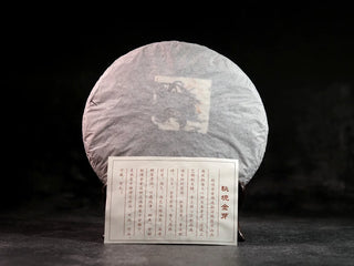Misty Gold Bud Ripe Pu-erh Tea Cake – Menghai First-Spring-tea cake unwrapped from outer packaging, still wrapped in white thin paper with a product information card displayed