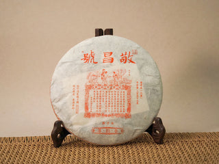 Jing Chang Hao Deep Velvet 2020 ripe Pu-erh cake wrapped in traditional paper with red product label, on a wooden stand
