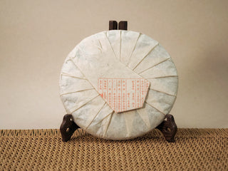 Jing Chang Hao Deep Velvet 2020 ripe Pu-erh cake in opened paper wrapper with red brand characters, on a wooden tea stand
