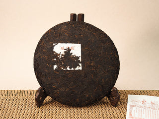 Front of Jing Chang Hao Deep Velvet 2020 ripe Pu-erh 357g cake with dark fermented leaves and white brand label on wooden stand