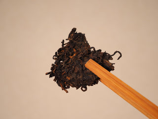 Loose chunk of Jing Chang Hao Deep Velvet 2020 ripe Pu-erh lifted with a bamboo tea pick before brewing