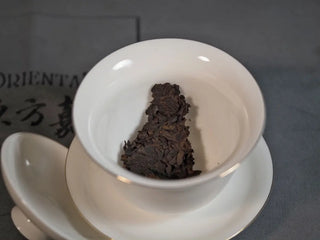 The pried-off Pu-erh chunk placed inside a white porcelain gaiwan before infusion