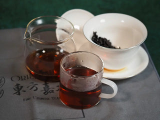 Glass fair cup, white gaiwan, and tasting cup displayed together with a close-up of the reddish tea liquor in the cup