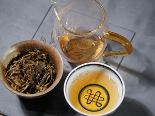 Top-down view of Hidden Mountain Raw Pu-erh Tea Cake (357g) brewing setup, including gaiwan, tea leaves, and poured tea in a sharing cup, displaying aroma and color.