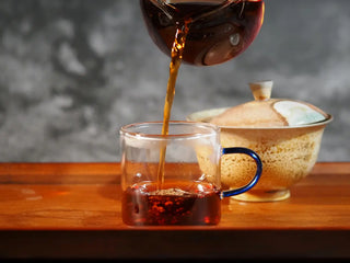 Mixiang 2017 Ripe Pu-erh Tea – MengHai Mid-Aged Golden Tip Pu-erh tea being poured from a fairness cup into a glass tasting cup, showing clear, warm amber-red tea liquor