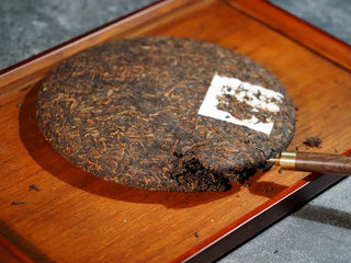 Mixiang 2017 Ripe Pu-erh Tea – MengHai Mid-Aged Golden Tip Pu-erh tea cake on a tea tray with a small piece of tea loosened using a tea pick