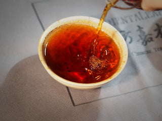 Spring Ming Ripe Pu-erh Tea Cake (2008 Commemoration) – Menghai, Yunnan pouring tea from gongdao cup into tasting cup, highlighting rich red-brown liquor ready for tasting.