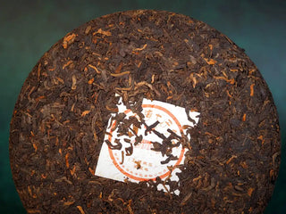 Spring Ming Ripe Pu-erh Tea Cake (2008 Commemoration) – Menghai, Yunnan front close-up showing shiny, dark brown tea leaves with intricate compressed patterns.