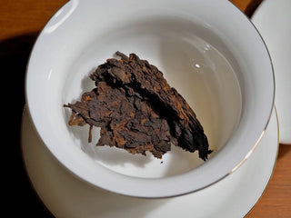 A portion of Spring Ming Large 400g Menghai Ripe Pu-erh Tea Cake – 2020 placed inside a white porcelain gaiwan ready to brew.