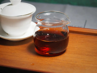 Bright, clear red liquor of the Spring Ming Large 400g Menghai Ripe Pu-erh Tea Cake – 2020 displayed in a glass fairness cup.